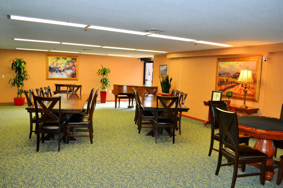 A well-lit dining area with multiple tables and chairs, decorated with paintings and a piano.