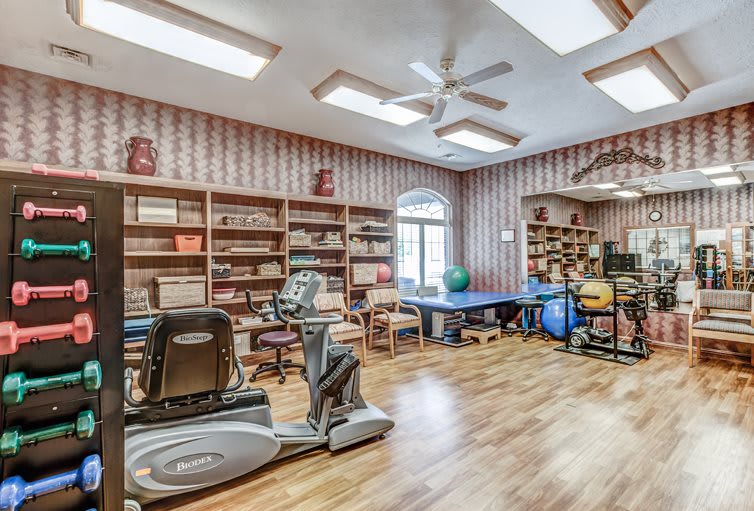 A well-organized exercise room with fitness equipment and wooden flooring.
