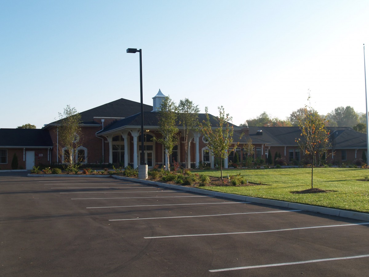 A large building with a parking lot, surrounded by trees on a sunny day.