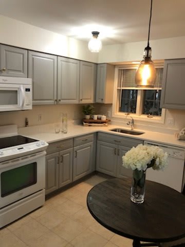 A cozy kitchen featuring gray cabinets, white appliances, and modern lighting with a vase of flowers on the table.