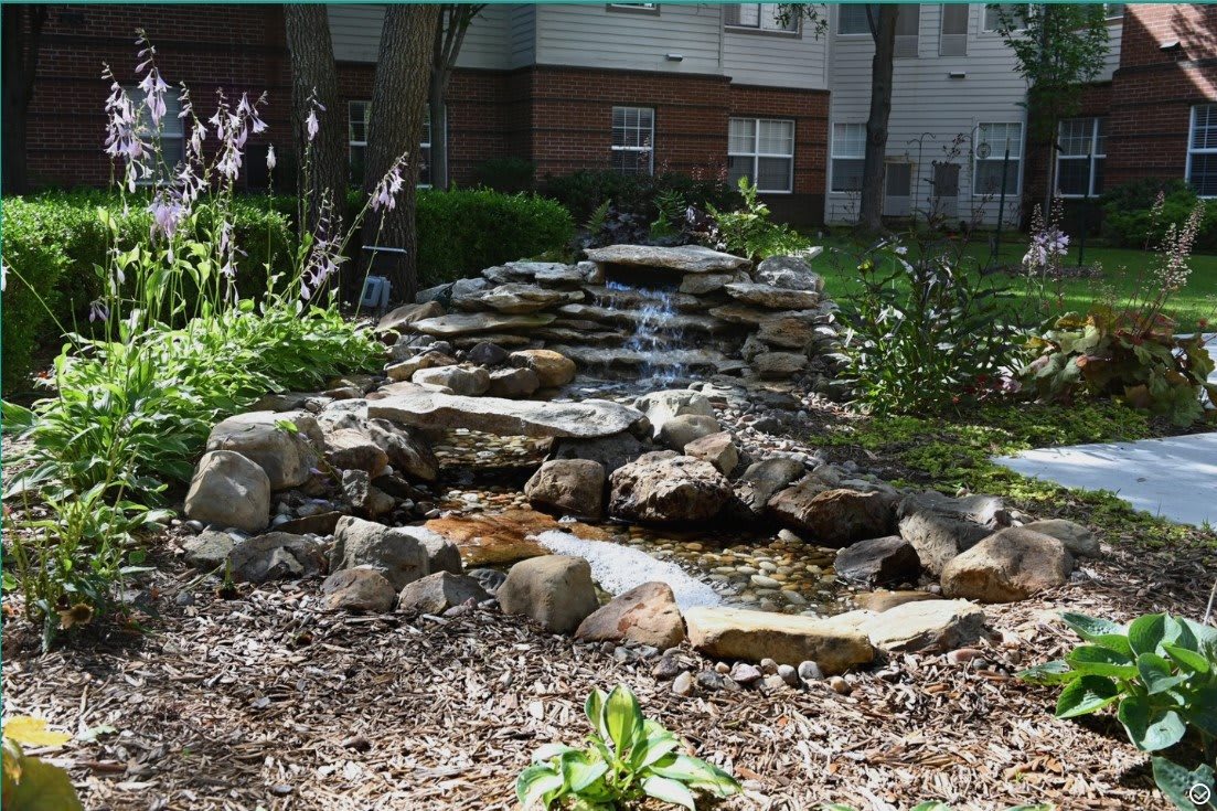A small waterfall cascades over rocks in a garden setting.