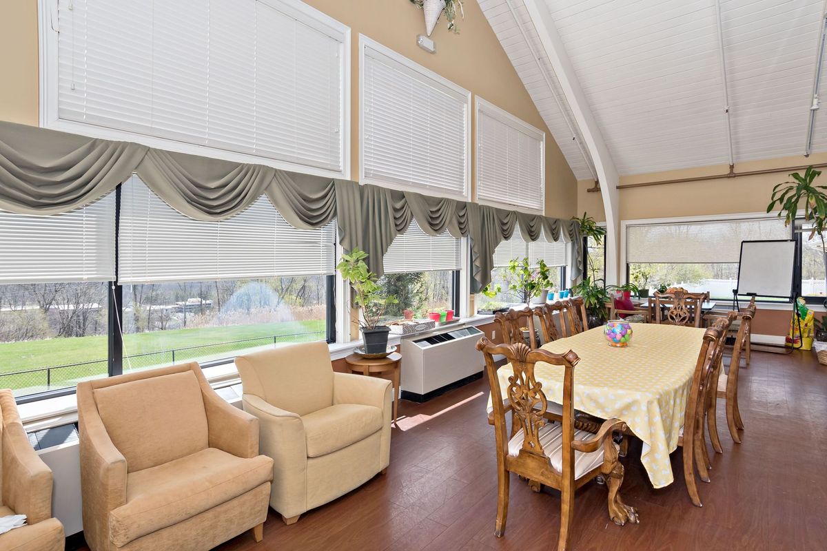 A spacious living and dining area featuring large windows with curtains, comfortable seating, and a dining table set.