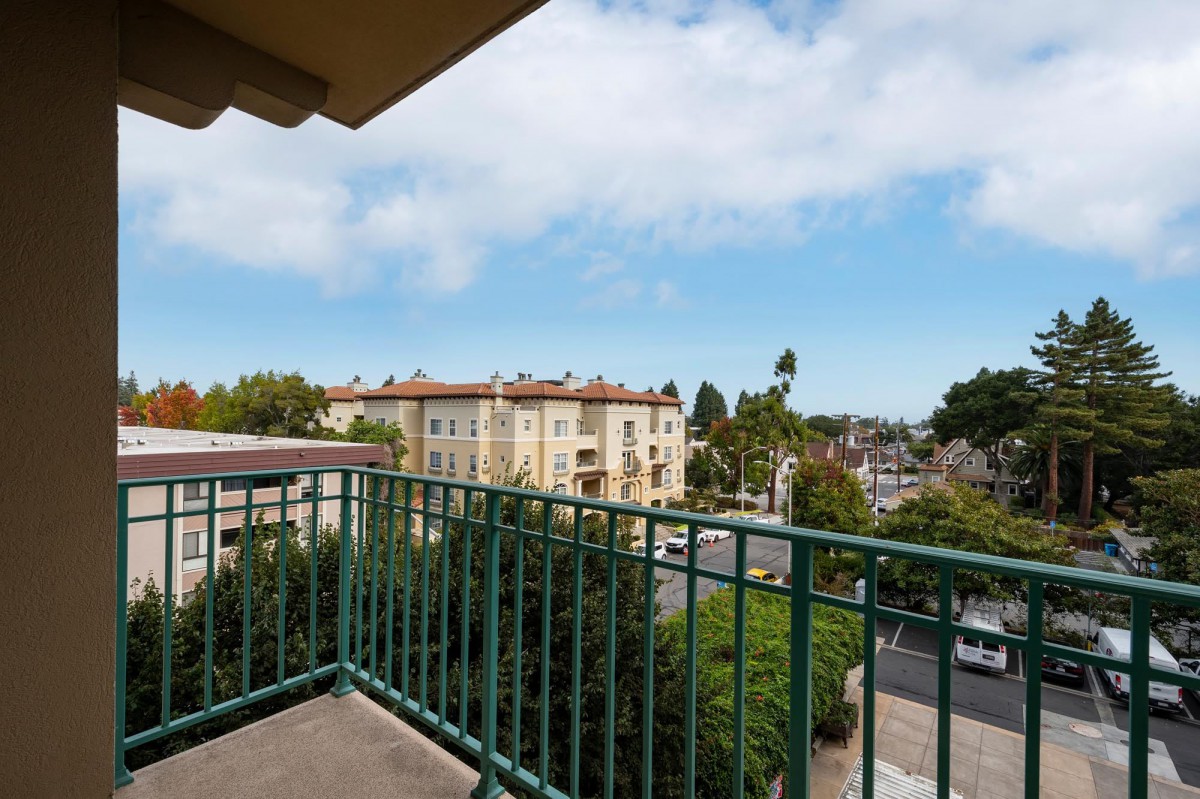 A balcony overlooking an urban scene with buildings and trees under a cloudy sky.