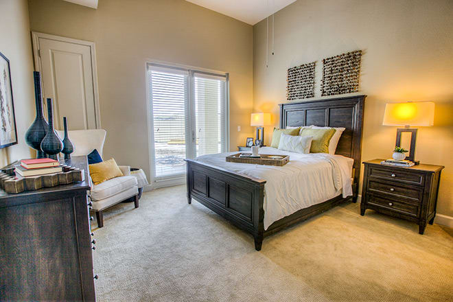 A cozy, well-decorated bedroom featuring a large bed with accent pillows, a lamp on the bedside table, and natural light streaming through a window.