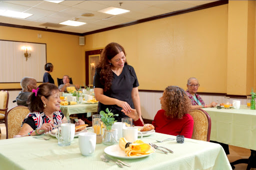 A staff member engages with a guest during a meal in a dining setting for seniors.