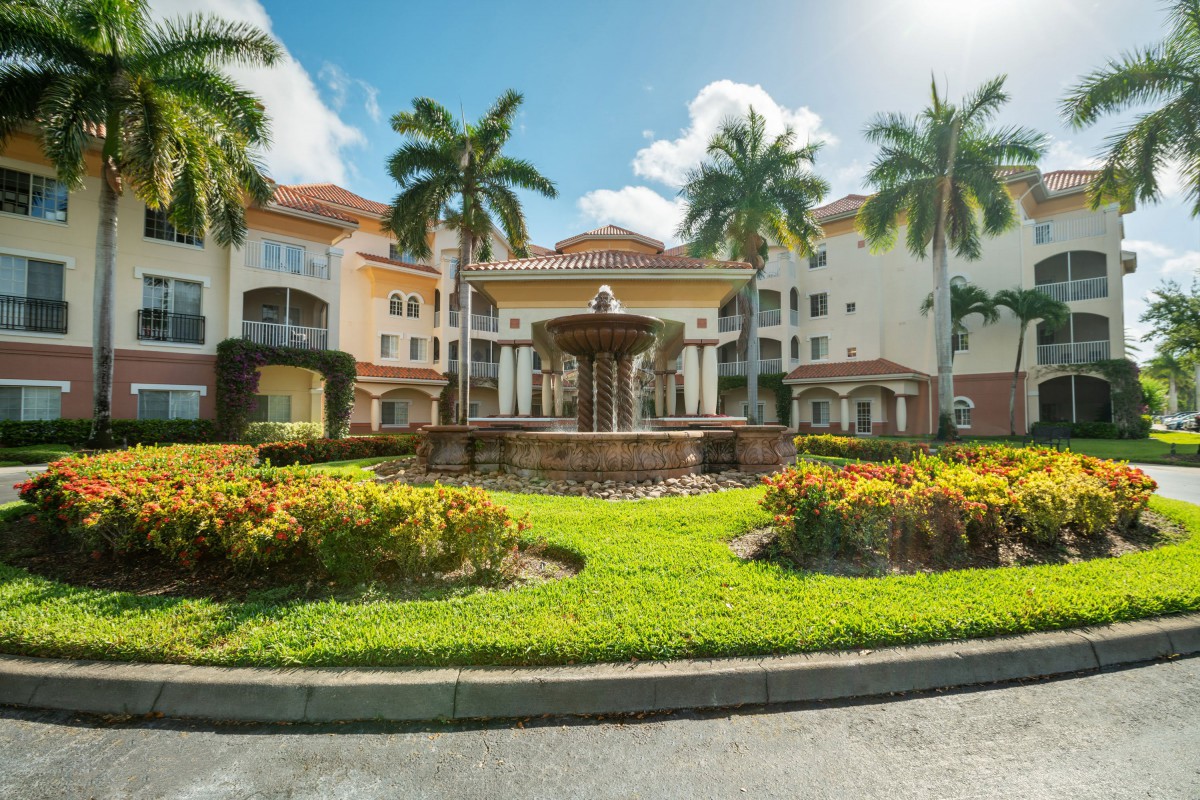 A luxurious residential building with a central fountain, surrounded by well-maintained landscaping and palm trees under a sunny sky.