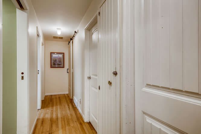 A well-lit hallway with wooden floors and several doors.