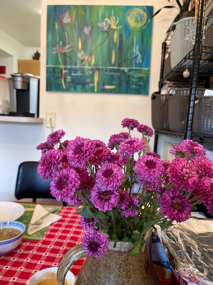 A vase of vibrant purple flowers on a table in a cozy interior setting.