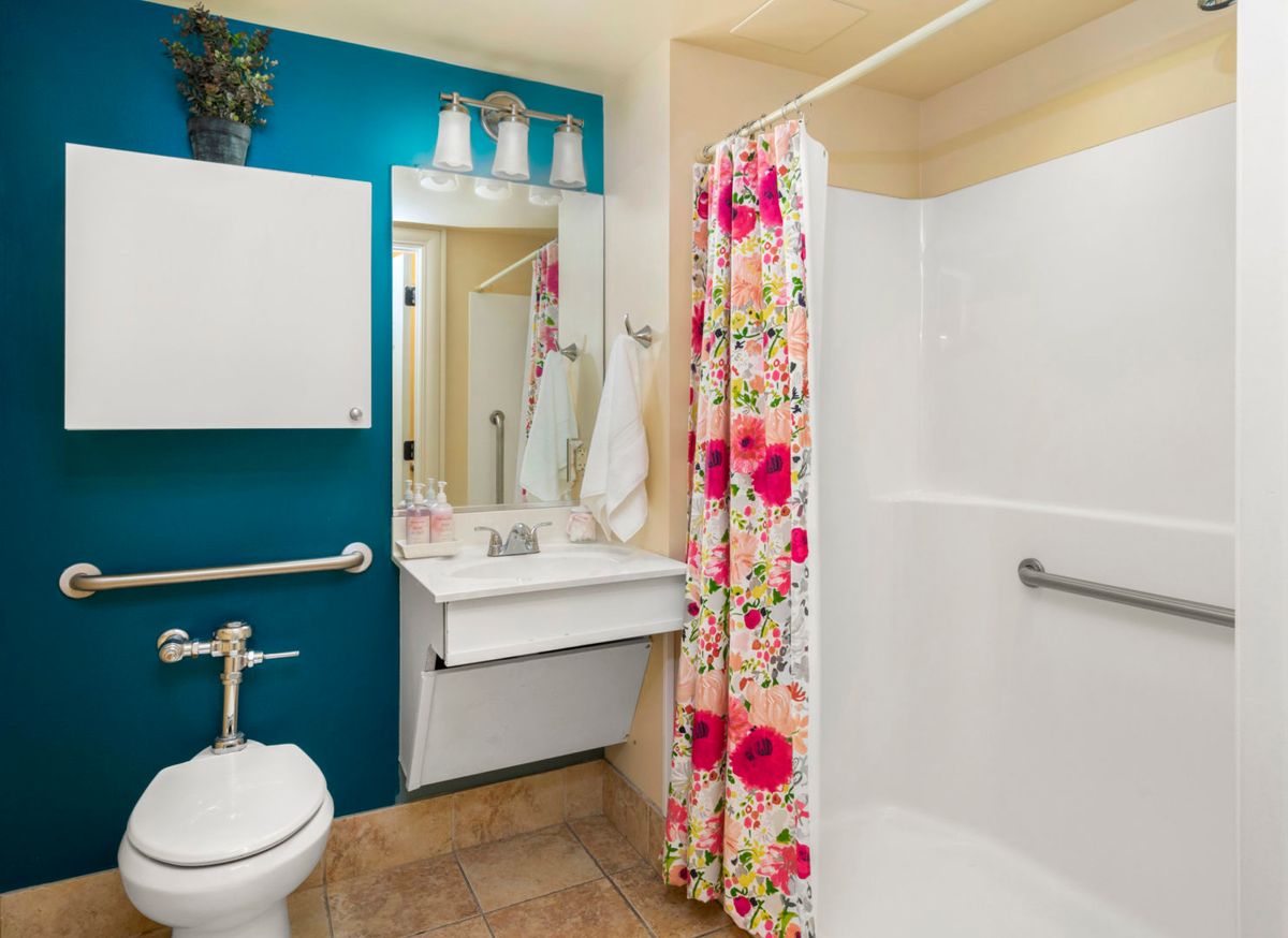 A cozy bathroom featuring a floral shower curtain and teal accent wall.