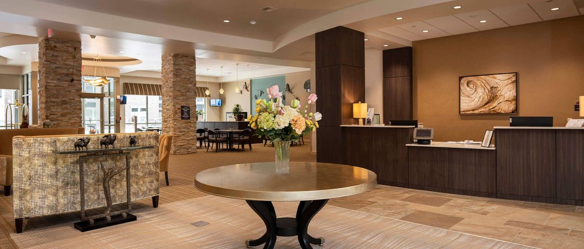 A modern hotel lobby featuring a round table with a floral arrangement and a reception desk.