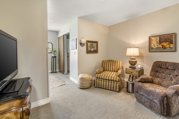 A cozy living room area featuring a striped armchair, a side table with a lamp, and classic decor.