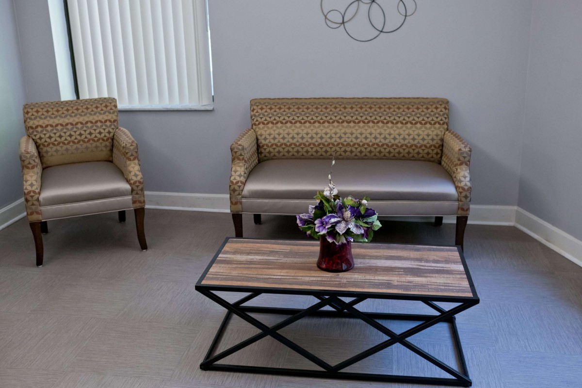 A cozy waiting room with comfortable chairs, a wooden table, and a floral arrangement.