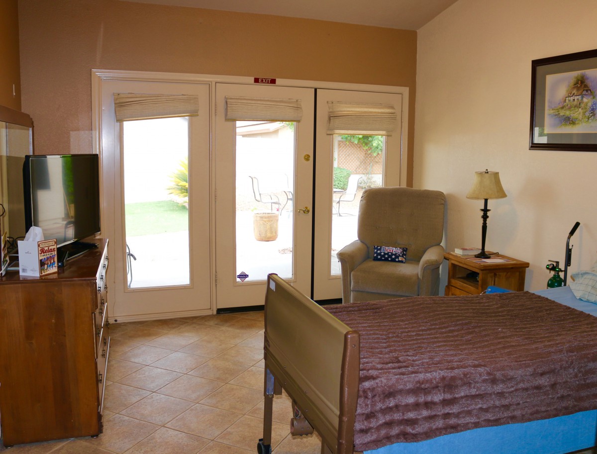 A cozy bedroom with a bed, armchair, and lamp near glass doors leading outside.