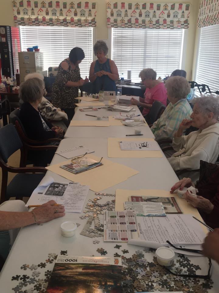 A group of elderly individuals participating in a crafting activity around a long table indoors.