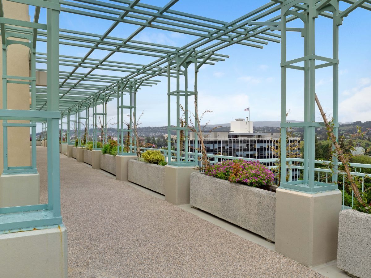 A pergola-covered walkway with views of the city and surrounding landscape.