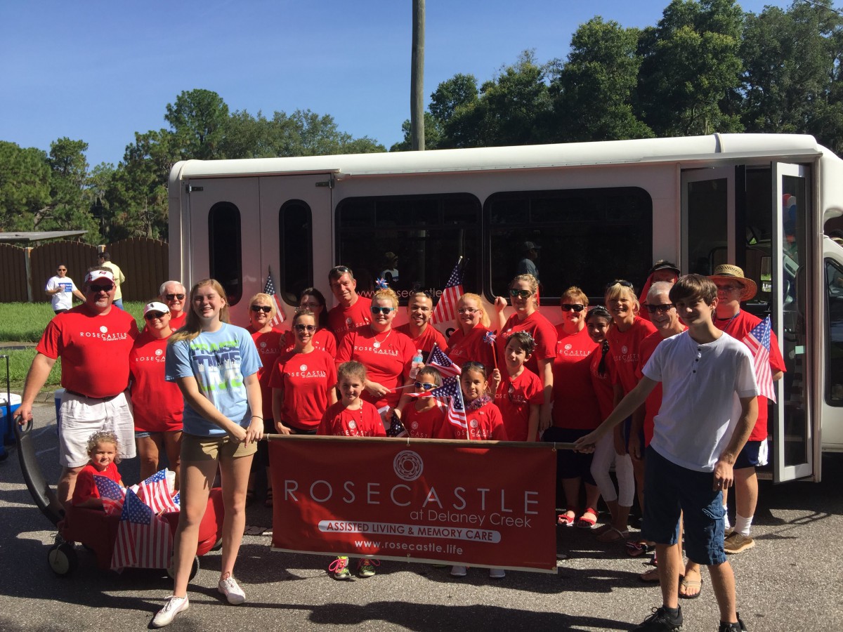 A group of people in red shirts pose with a banner outdoors, possibly as part of a parade or team event.