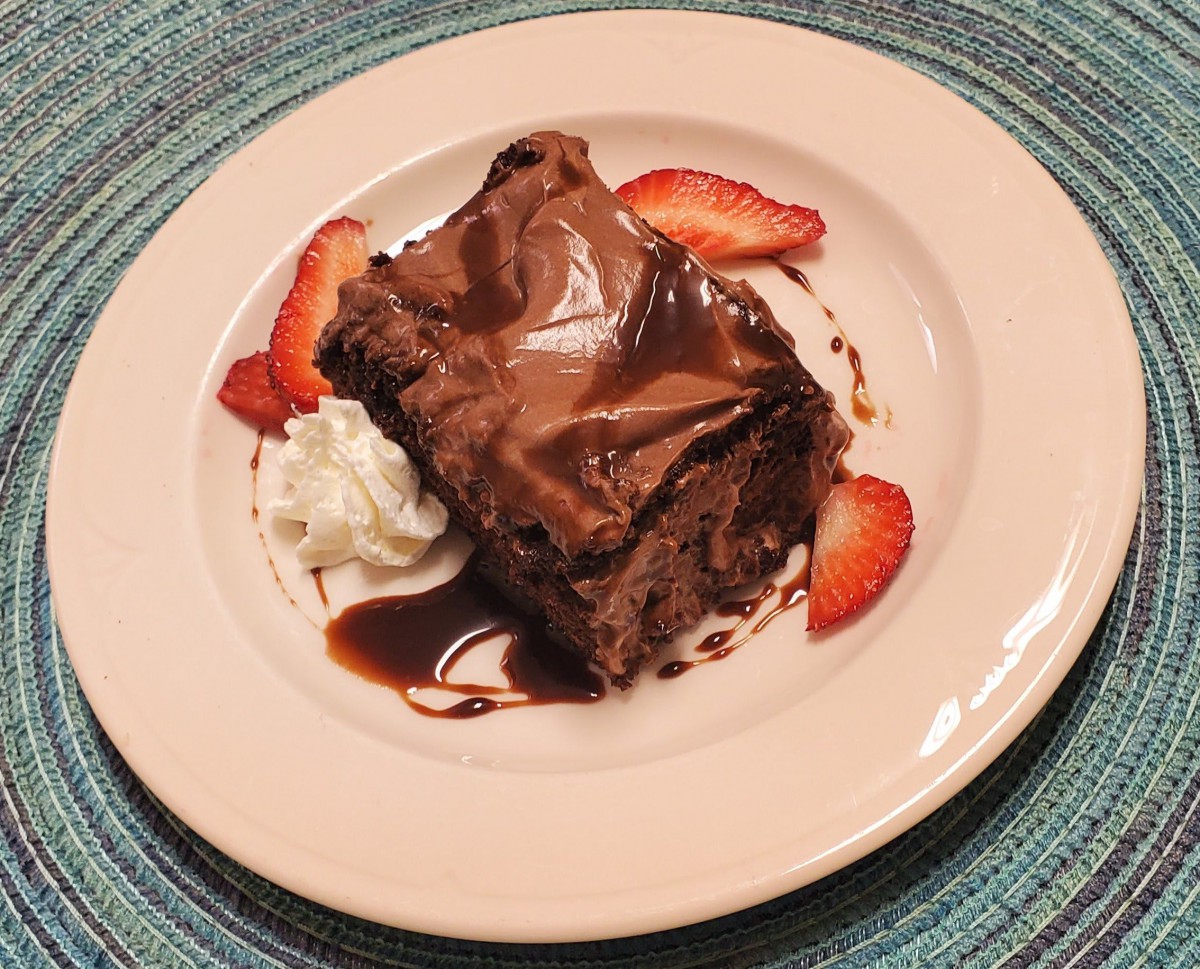 A slice of chocolate cake served with strawberries and whipped cream, drizzled with chocolate sauce.