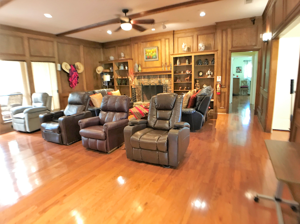 A cozy living room with several recliner chairs, wood paneling, a fireplace, and decorative shelves.