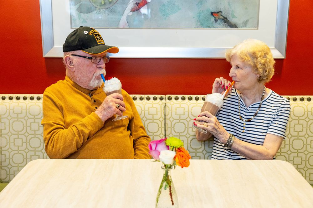 An elderly couple enjoying ice cream together at a table with flowers.