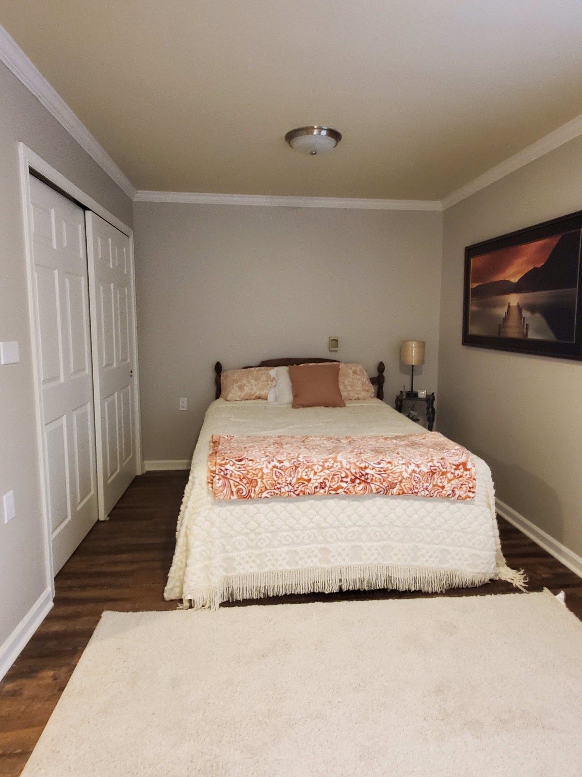 A cozy bedroom with a neatly made bed, artwork on the wall, and a lamp on the bedside table.
