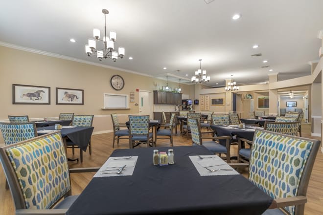 A spacious dining area with neatly arranged tables and chairs, well-lit by elegant chandeliers.