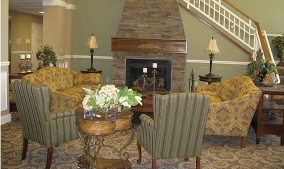 A cozy living room featuring a stone fireplace, armchairs, and a small table with a floral arrangement.