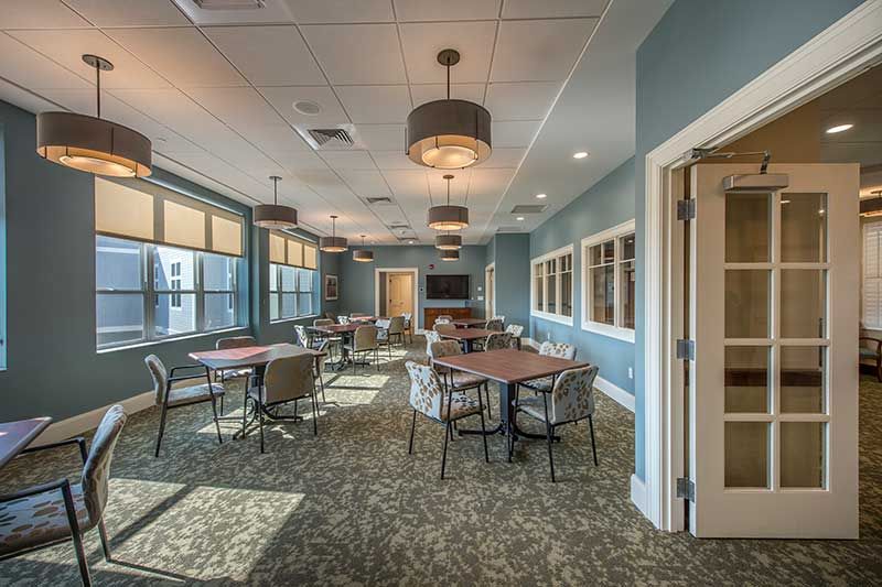 A spacious meeting room with tables, chairs, and large windows providing natural light.