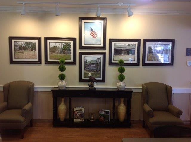 A waiting room interior featuring framed artwork, two chairs, and decorative plants.