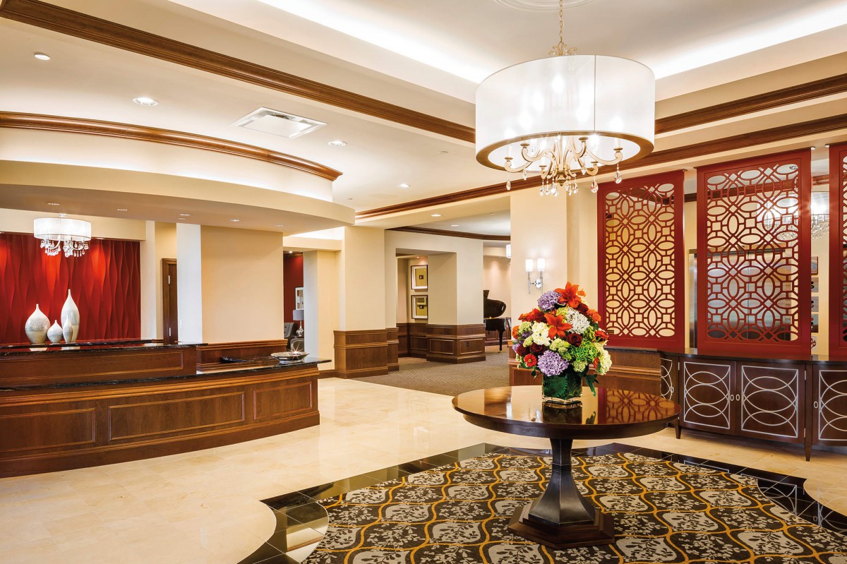 A luxurious hotel lobby with elegant decor, featuring a chandelier and floral arrangement.
