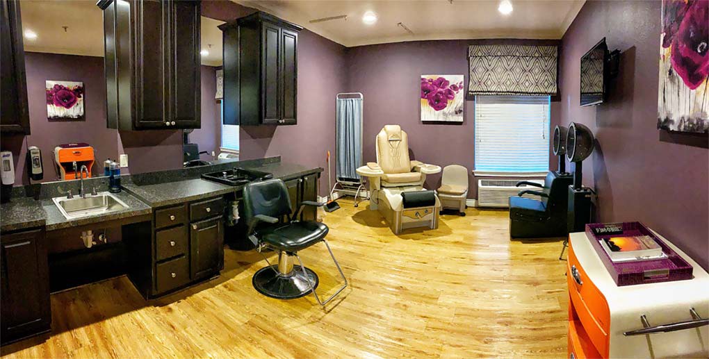 A well-equipped salon interior featuring a hairdressing chair and massage chair with purple walls and wooden flooring.