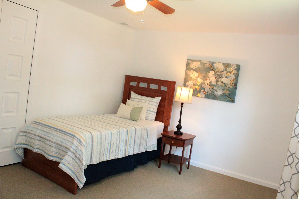 A minimalist bedroom featuring a single bed with striped bedding, a nightstand with a lamp, and a piece of artwork on the wall.