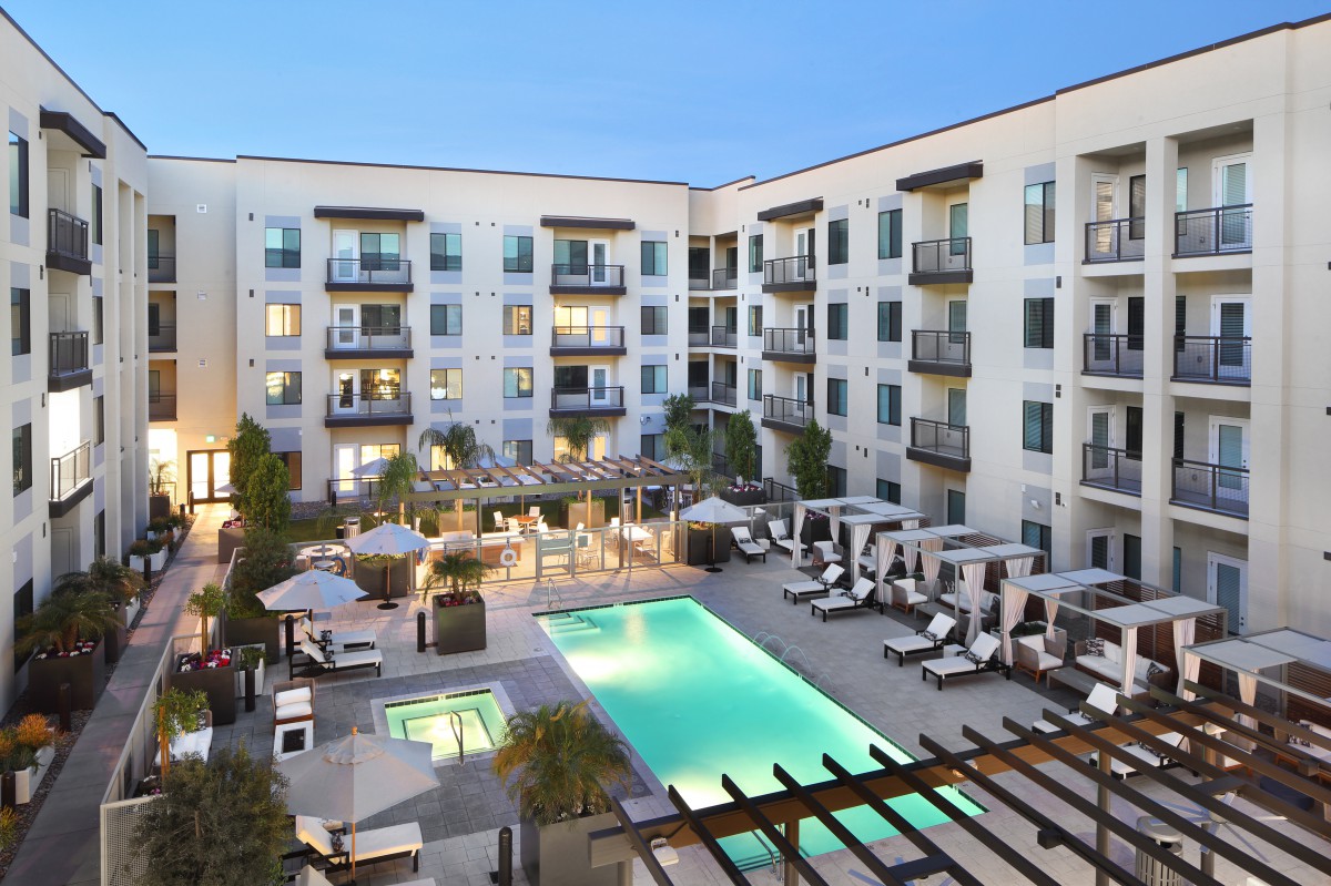 A modern apartment complex with a central swimming pool and outdoor lounging area during the evening.