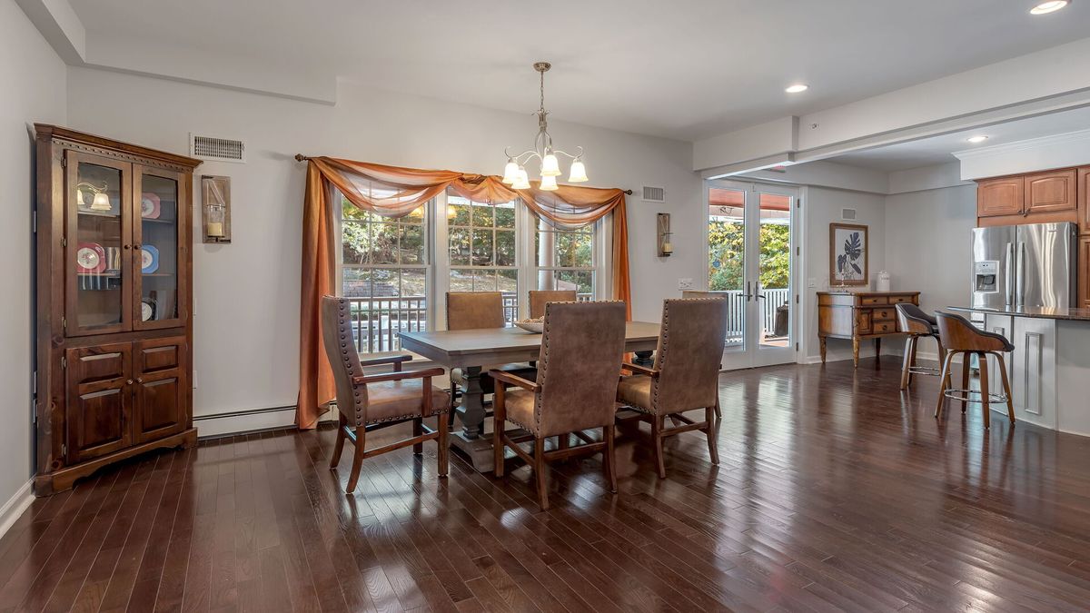 A spacious dining room with a wooden table, chairs, and a chandelier, featuring hardwood floors and large windows that allow in natural light.