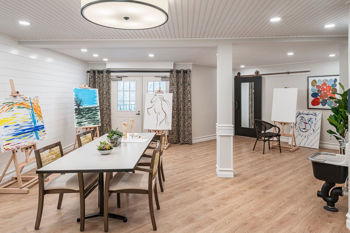 A modern multipurpose room featuring a conference table, chairs, and art easels.