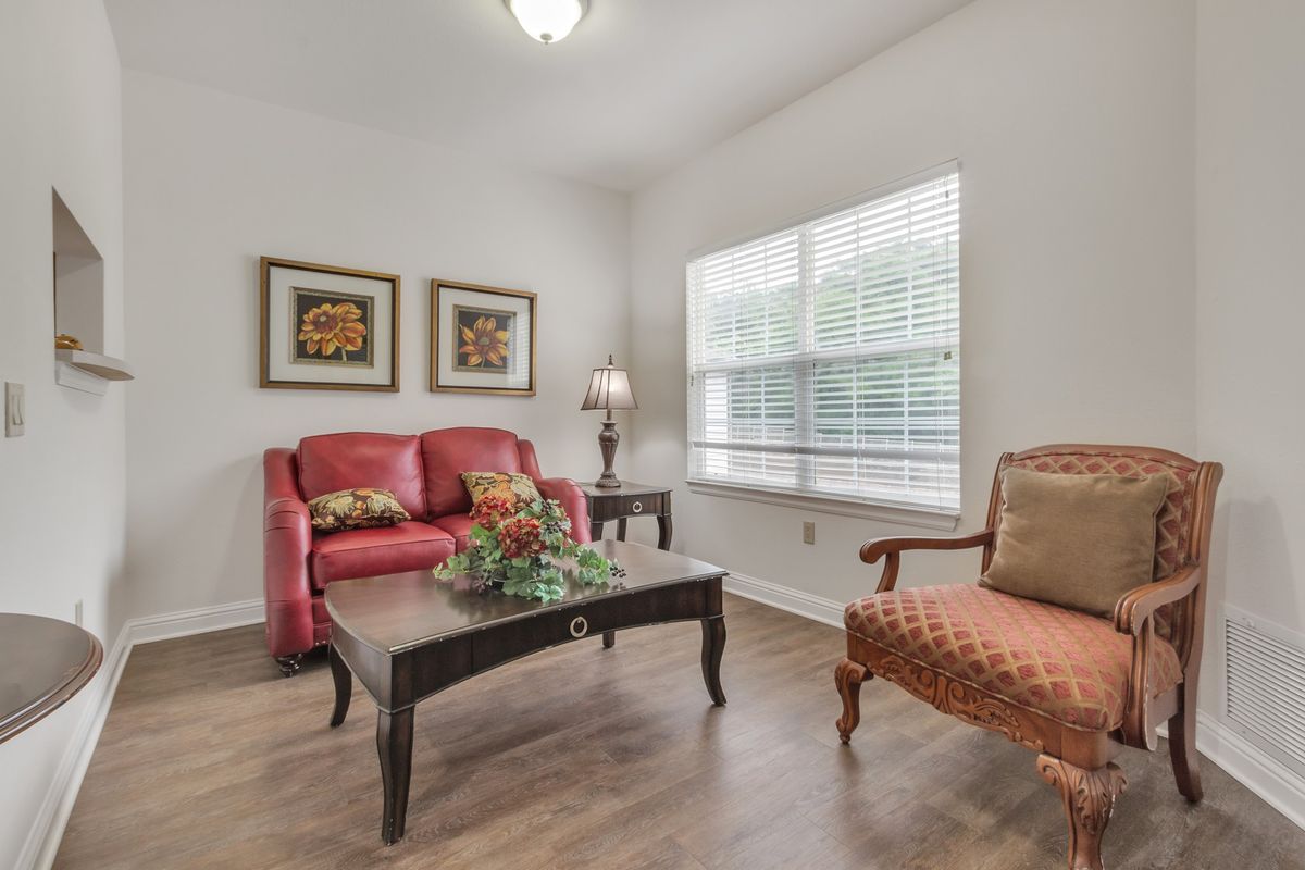 A cozy living room with a red sofa and an orange armchair, featuring a coffee table and wall art.