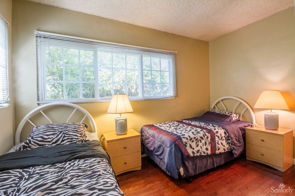 A cozy bedroom with two single beds, a nightstand, and a window providing natural light.