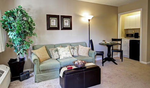 A cozy living room with a green sofa, wall art, and a lamp beside a round dining table.