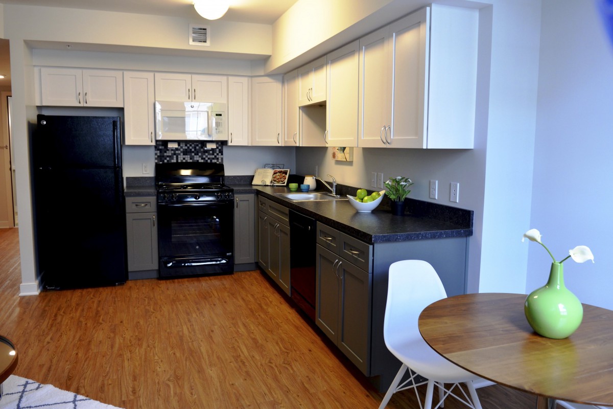 A modern kitchen with black and white cabinetry, dark countertops, and wooden flooring.