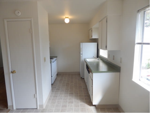 A compact kitchen with white walls, featuring a refrigerator and stove.