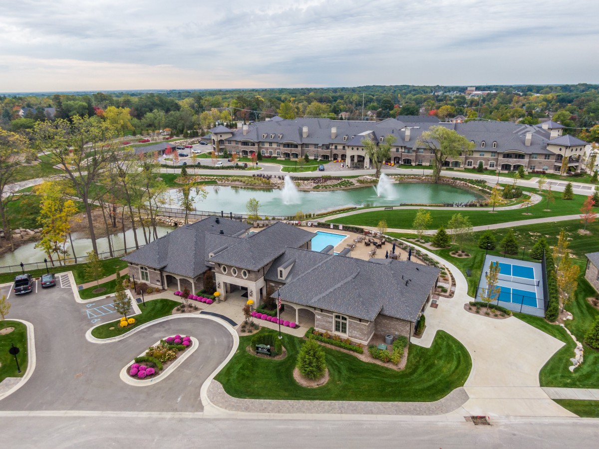 An aerial view of a residential community featuring landscaped gardens, fountains, a clubhouse, and a tennis court.