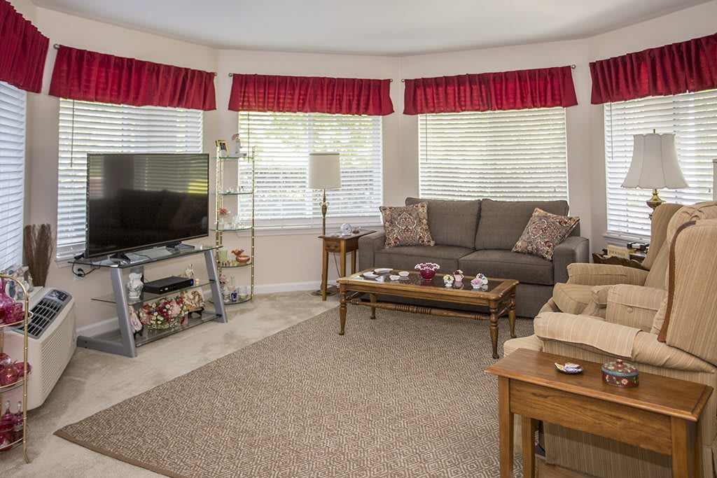 A cozy living room with a sofa, television, and a coffee table surrounded by windows with red curtains.