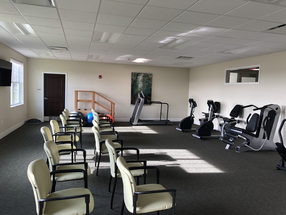 A well-lit gym with rows of chairs and various exercise equipment, including treadmills and stationary bikes.