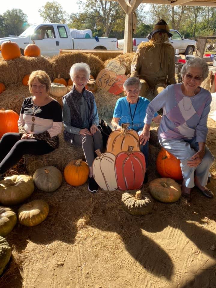 A group of women sitting among pumpkins and hay bales, enjoying a sunny autumn day.