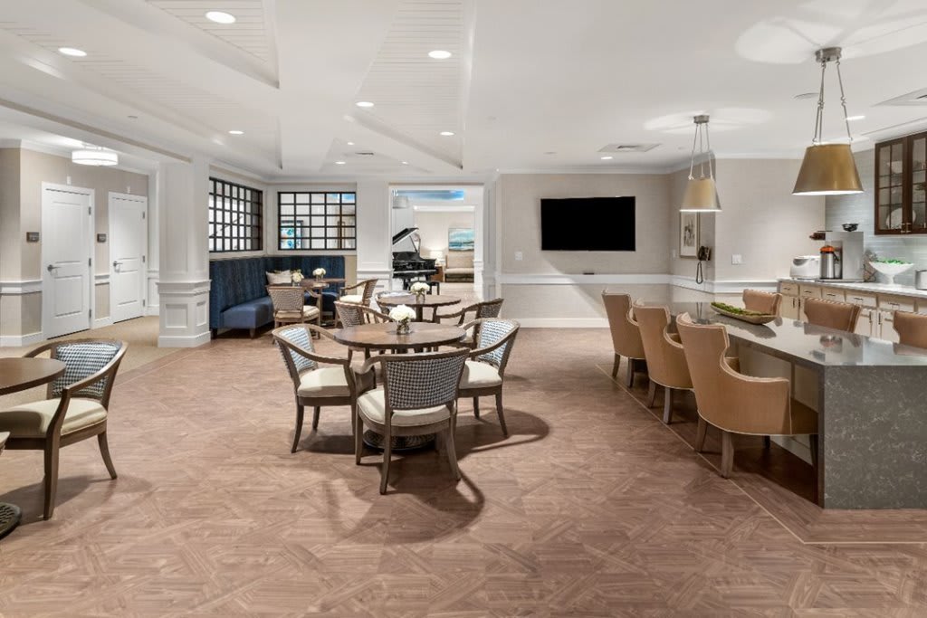A modern and elegant lounge with dining tables, comfortable seating, and a large television on the wall.