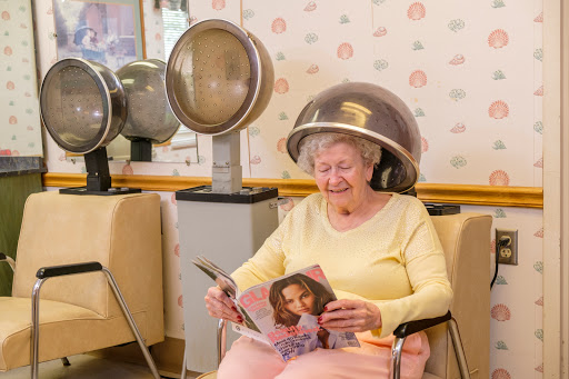 An elderly woman enjoys reading a magazine while undergoing a beauty treatment at a hair salon.
