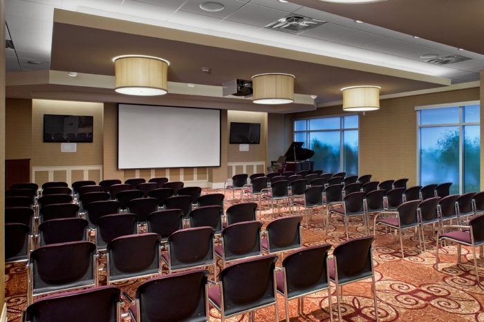 An empty conference room with rows of chairs facing a projector screen, set up for a meeting or presentation.