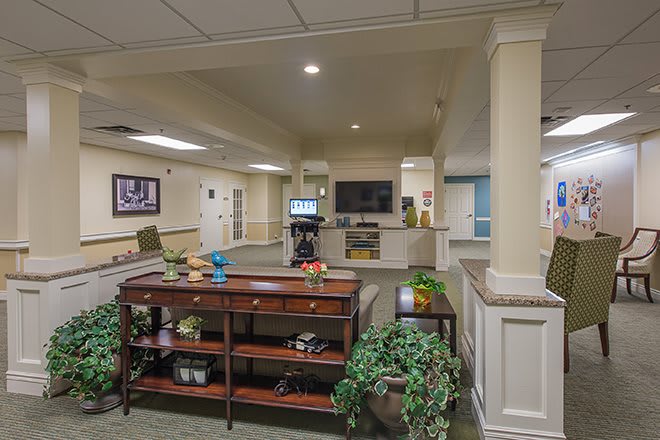 A spacious lobby area with a central table, potted plants, and a reception desk in the background.