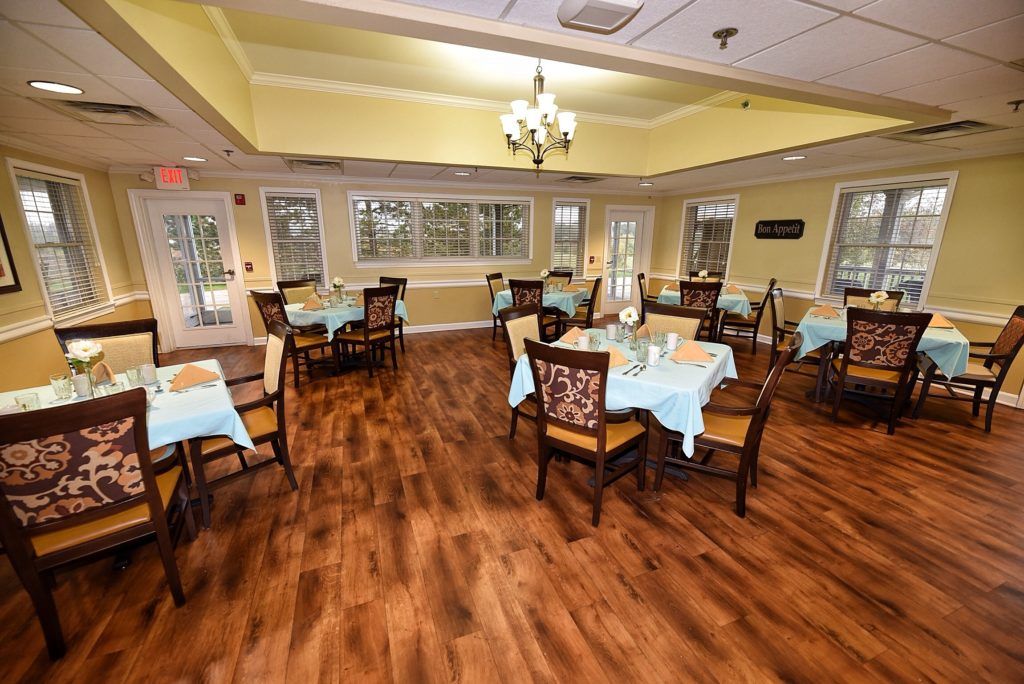 A cozy dining room with neatly arranged tables and chairs, featuring a wooden floor and chandelier.