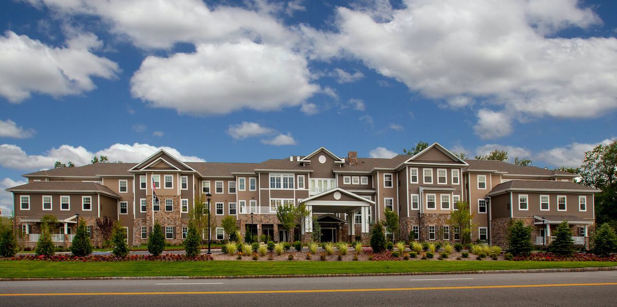 A large residential building under a blue sky with clouds, surrounded by landscaping and trees.