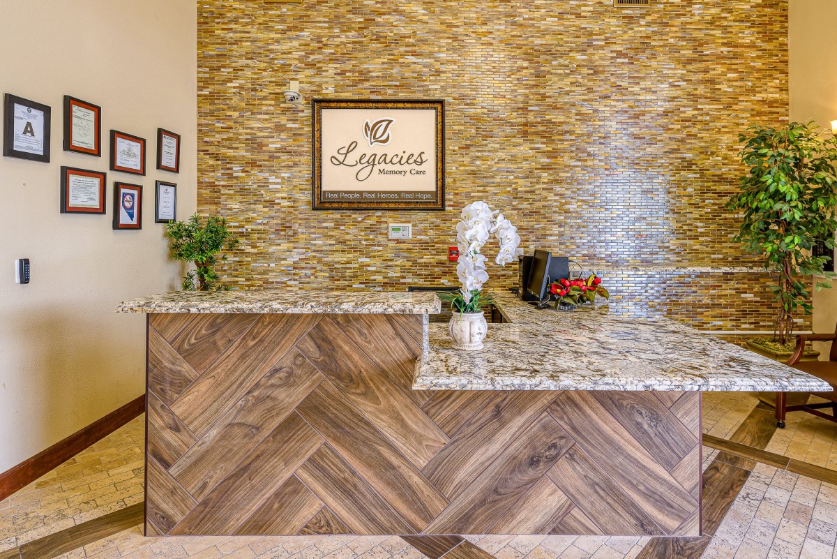 A welcoming reception area with wood paneling and a granite countertop, adorned with decorative plants and signage.